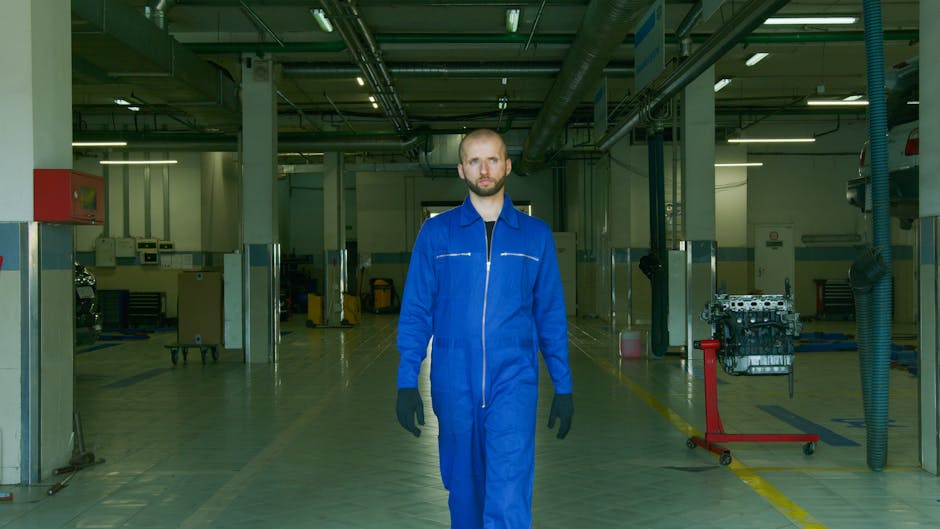 A mechanic wearing a blue jumpsuit walks confidently through a modern auto workshop.